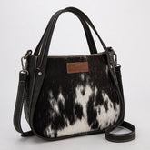 Wrangler genuine hair-on cowhide crossbody and tote bag in black, featuring natural cowhide texture, dual top handles, adjustable shoulder strap, and rustic Western leather patch