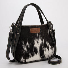 Wrangler genuine hair-on cowhide crossbody and tote bag in black, featuring natural cowhide texture, dual top handles, adjustable shoulder strap, and rustic Western leather patch
