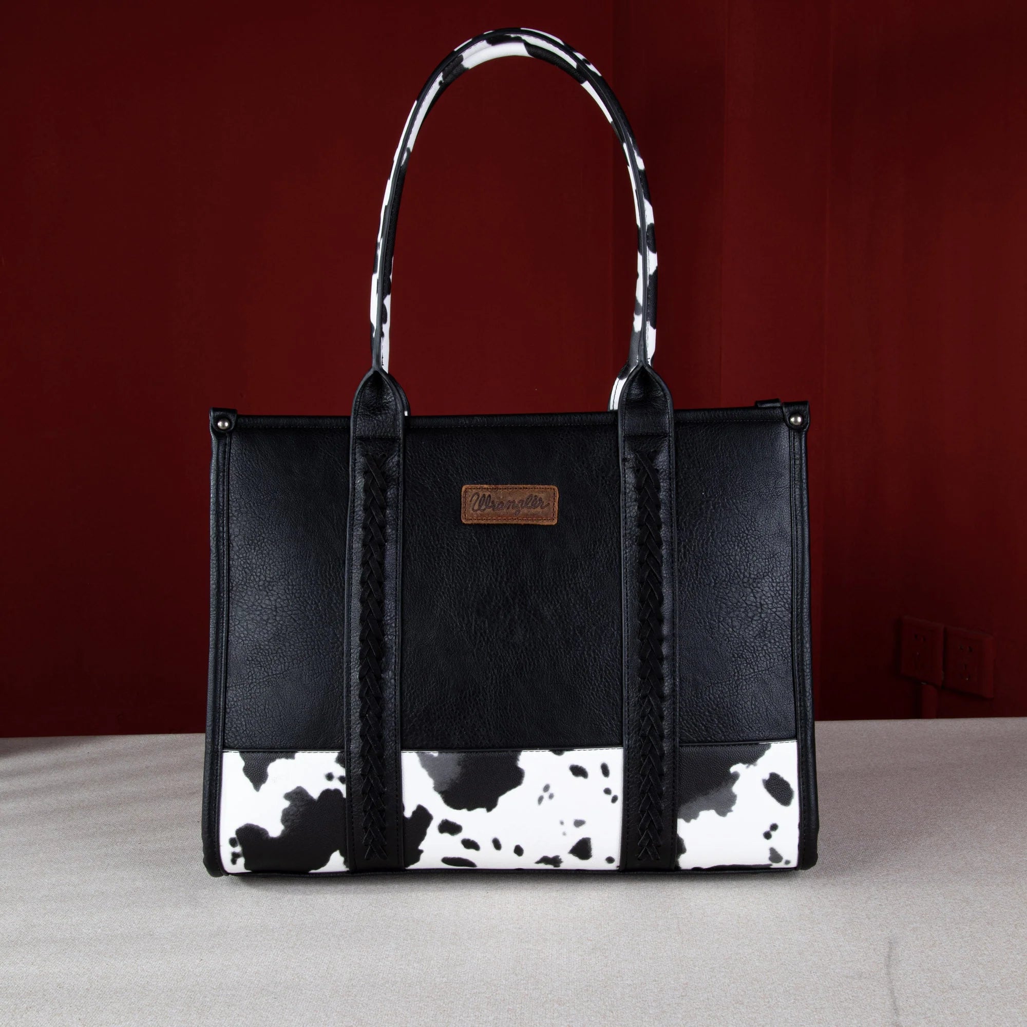Wrangler cow print purse in color black with concealed carry pocket, whipstitch details, and signature Wrangler logo. Secure zipper top. 
