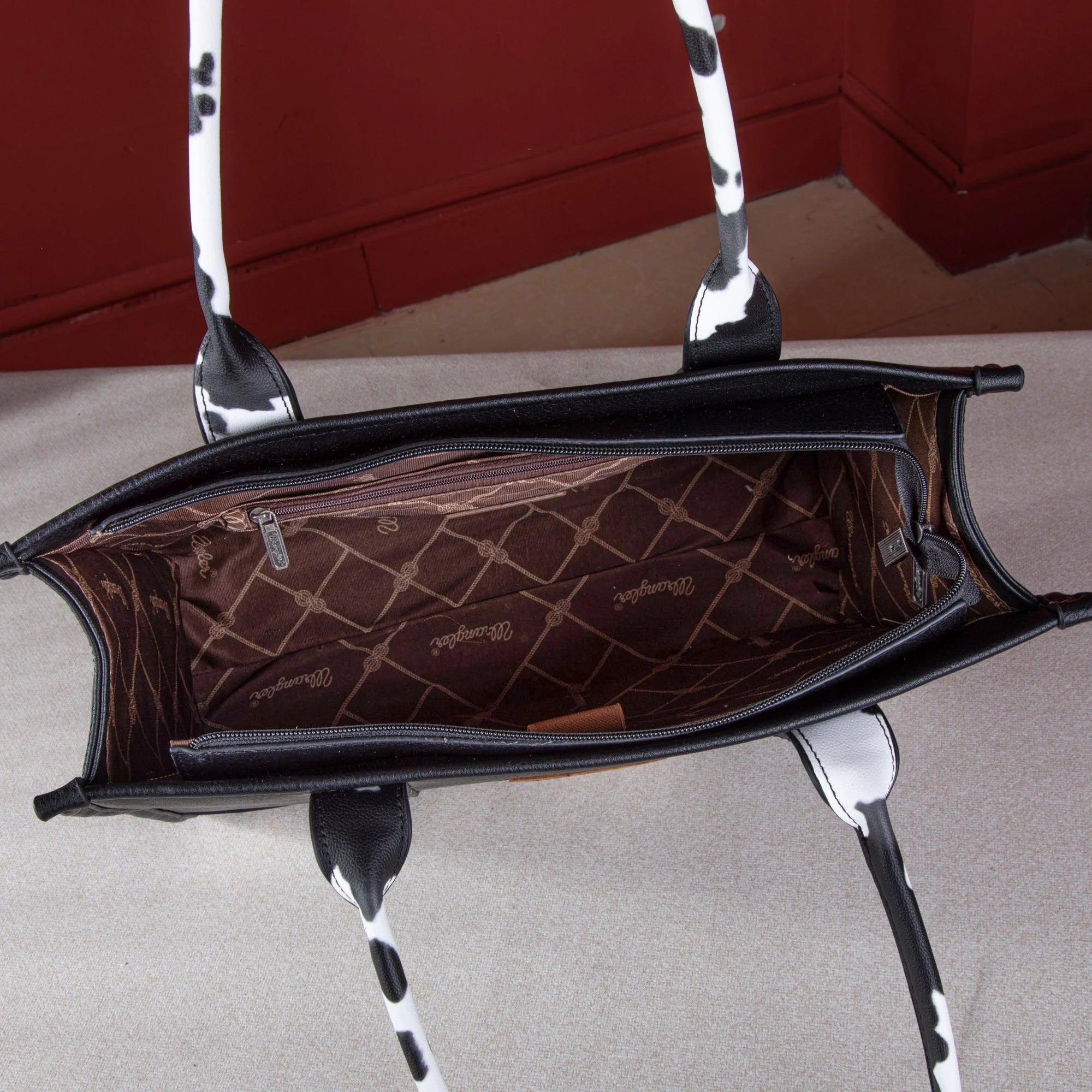 Interior view of the Wrangler cow print purse in black, showcasing spacious compartments and signature branded lining—ideal for Western cowgirls seeking both style and function.

